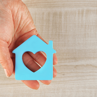 Female hand with model of house on wooden table background