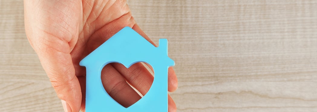 Female hand with model of house on wooden table background